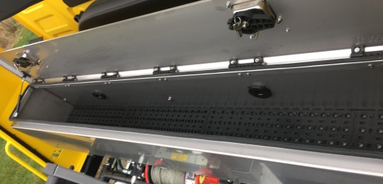 Un coffre à outils en inox avec ouverture par le dessus sur toute la largeur positionné sur la traverse du roll-bar